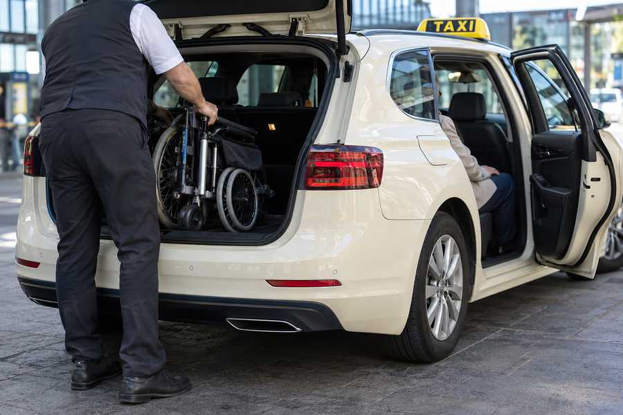 Fahrer lädt einen Faltrollstuhl in den Kofferraum des Taxis